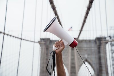 A hand holding a megaphone into the air, a suspension bridge in the background