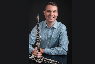 Bryce Newcomer, wearing a blue and white patterned shirt, with two clarinets