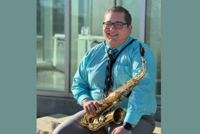 Daniel Gaete sits outdoors, holding a saxophone, wearing a blue shirt.