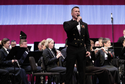 Wind players and a singer from the US Navy Band on stage in a performance