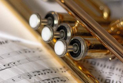 A closeup of the valves of a trumpet laying on top of sheet music
