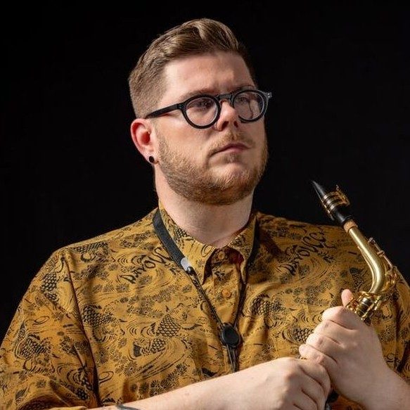 Kyle Hutchins, wearing a gold colored shirt, holding a saxophone