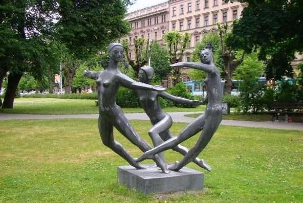  The image shows an outdoor sculpture of three naked women dancing in a circle. 