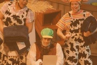 Actors dressed like farm animals gathered around a typewriter on stage. 