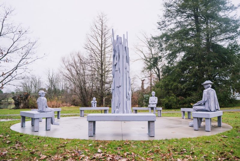 A sculpture where four life-sized human figure sculptures sit in contemplative and meditative poses on the benches.