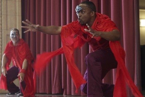 Two students with Rehabilitation Through the Arts perform in a theatre production wearing red costumes.