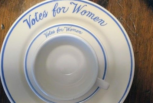 A white cup and saucer, sitting on a white plate, with the words 'Votes for Women' written on it