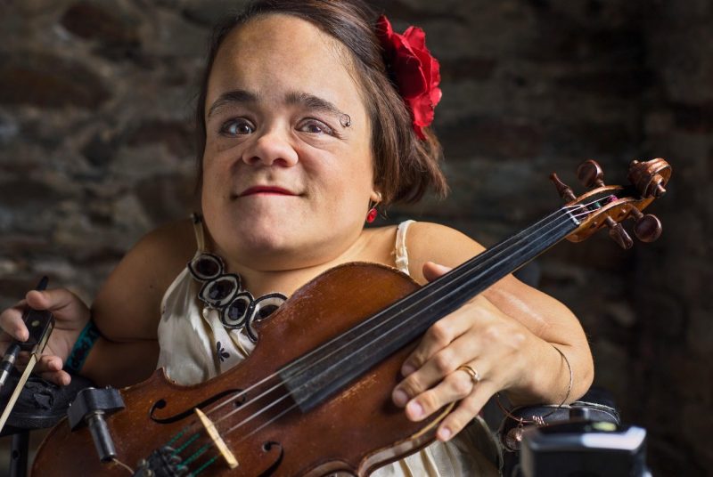 Violinist singer-songwriter Gaelynn Lea holds a violin in her lap and holds a bow in one hand.
