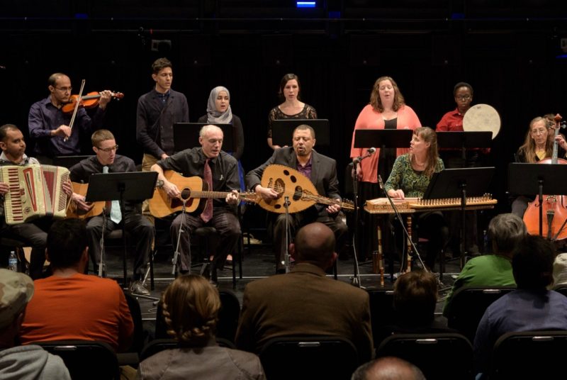Musicians in the Itraab middle eastern music ensemble sit onstage with various instruments.