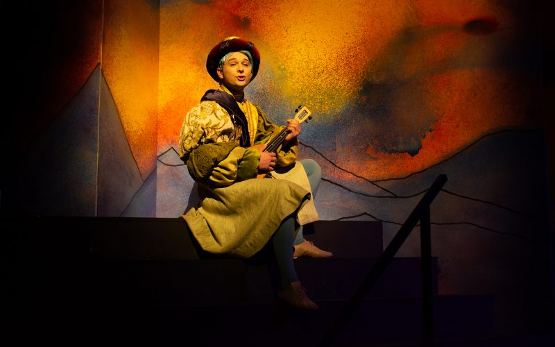 Student in a play singing with instrument on stage.