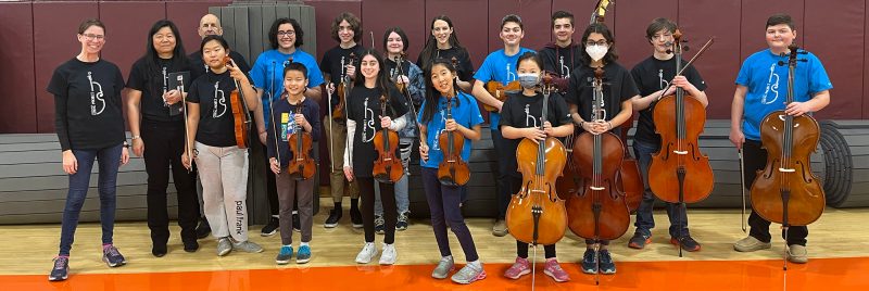 String Project staff and students pose together with instruments at event.