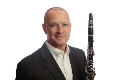 James Tobin headshot of a male in a dark jacket holding a clarinet.